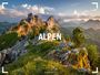 „ALPEN 2027“ steht im Vordergrund einer malerischen Berglandschaft mit felsigen Gipfeln und üppigem Grün im Abendlicht.