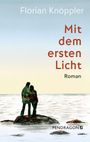 "Florian Knöppler, Mit dem ersten Licht, Roman. Zwei Personen umarmen sich auf einem Felsen am Wasser vor hellem Himmel."