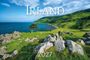 Text: "Stefan Schnebelt, Irland, 2027." Küstenlandschaft mit grünem Hügel, Felsen und blauem Meer unter einem bewölkten Himmel.