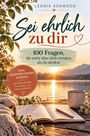 „Sei ehrlich zu dir. 100 Fragen, die mehr über dich verraten, als du denkst.“ Notizbuch und Tasse am See im Sonnenuntergang.
