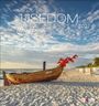 USEDOM, Meine Insel 2027. Ein Holzboot mit roten Fahnen am Sandstrand vor blauem Himmel mit Wolken.