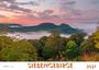 Text: "SIEBENGEBIRGE 2027". Nebel über grünen Hügeln mit einem leuchtenden Himmel bei Sonnenuntergang.