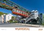 "WUPPERTAL 2027" in orange Schrift. Die Schwebebahn fährt über die Straße, modernes und historisches Design vermischt.