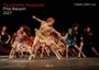 "Tanztheater Wuppertal, Pina Bausch, 2027" in weiß/rot. Tänzer in bunten Kleidern in dynamischer Pose auf Bühne.