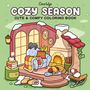 „COZY SEASON: CUTE & COMFY COLORING BOOK“ steht oben. Eine gemütliche Illustration zeigt ein Zimmer mit Kamin und Sessel.