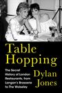 „Table Hopping“; Autor: Dylan Jones. Zwei elegant gekleidete Frauen bei einem Tischgespräch, Getränke und Lachen.